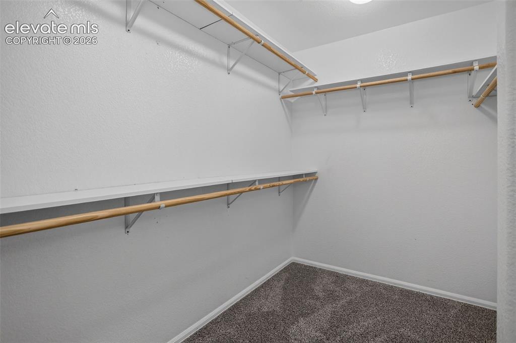 Image 22 of 46: Wall-mounted shelving system with hanging rods, bright white walls, and gra
