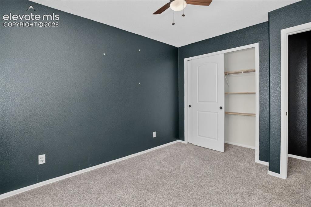 Image 23 of 46: Textured accent wall, ceiling fan, carpet flooring, sliding closet door, bu