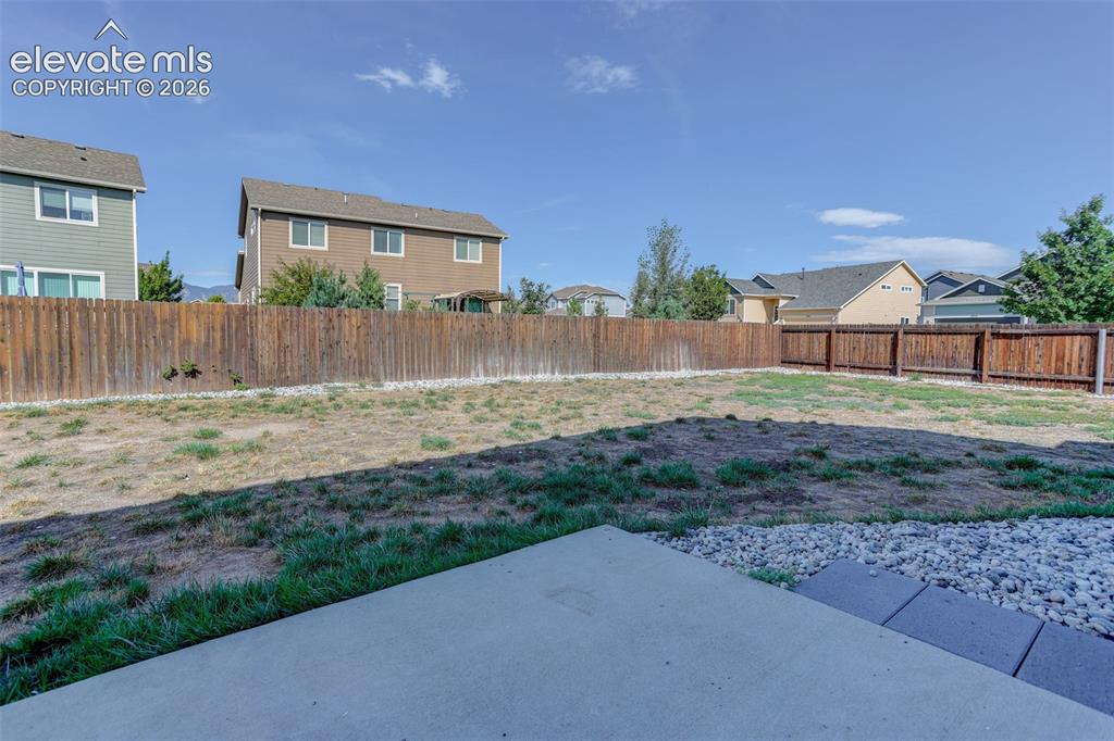 Image 39 of 46: Concrete patio with stone detailing, leading to an expansive fenced yard