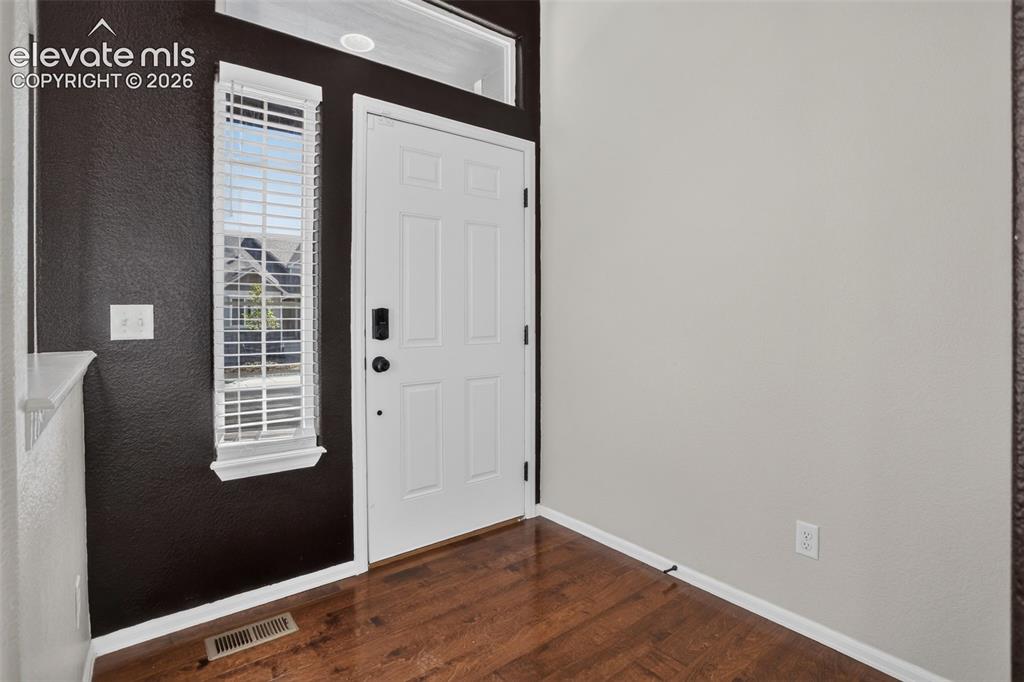 Image 6 of 46: Entryway featuring a white paneled door, sidelight with blinds, wood-finish