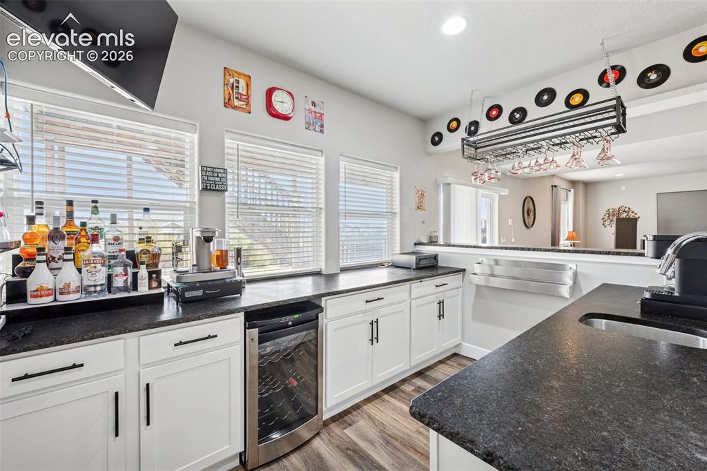 Image 32 of 40: Basement wet bar/kitchen has a wine cooler, white cabinets, easy care wood-