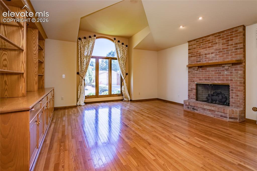 Image 11 of 40: Spacious room featuring wood-finish flooring, a prominent brick fireplace w