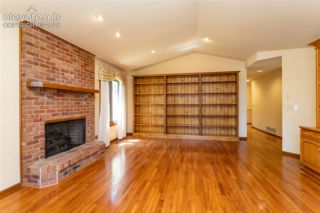Image 12 of 40: Spacious living area featuring polished wood-finish flooring, a brick firep