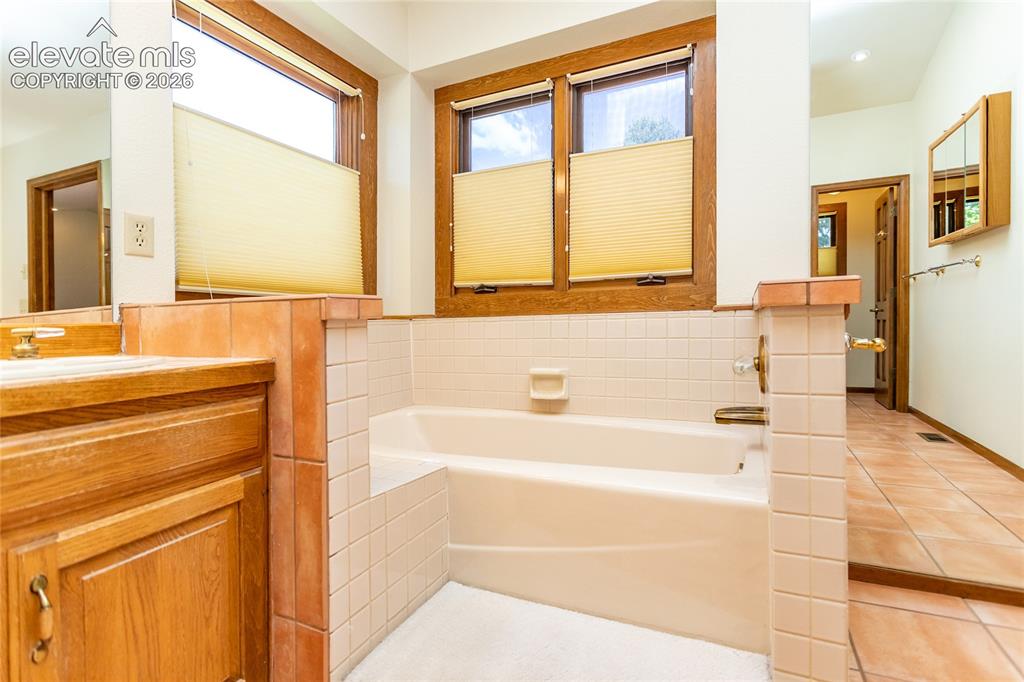Image 17 of 40: Bathroom featuring a built-in tub with white tile surround, wood-framed win