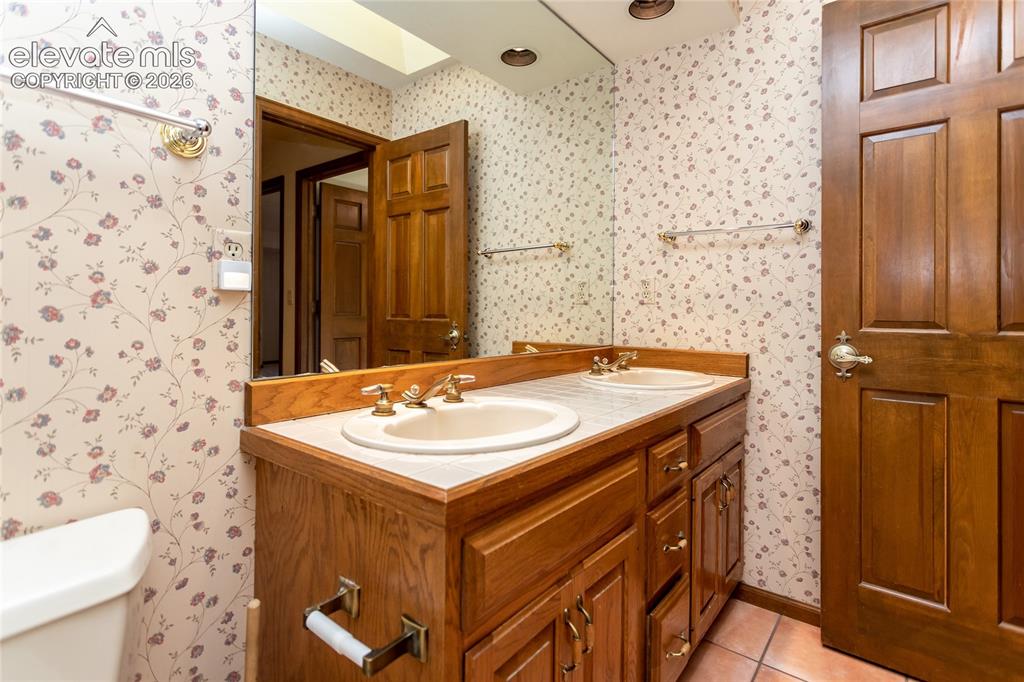 Image 25 of 40: Bathroom featuring a dual vanity with integrated sinks and brass-finish fau