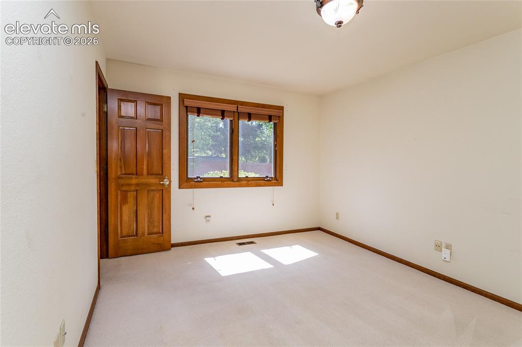 Image 26 of 40: Neutral-toned carpeted room featuring a six-panel wood door, wood window tr