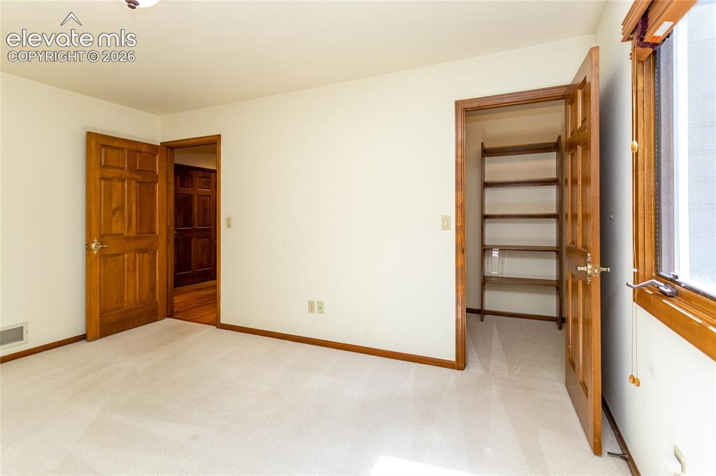 Image 27 of 40: Carpeted room featuring a built-in shelving unit, natural wood-finish doors