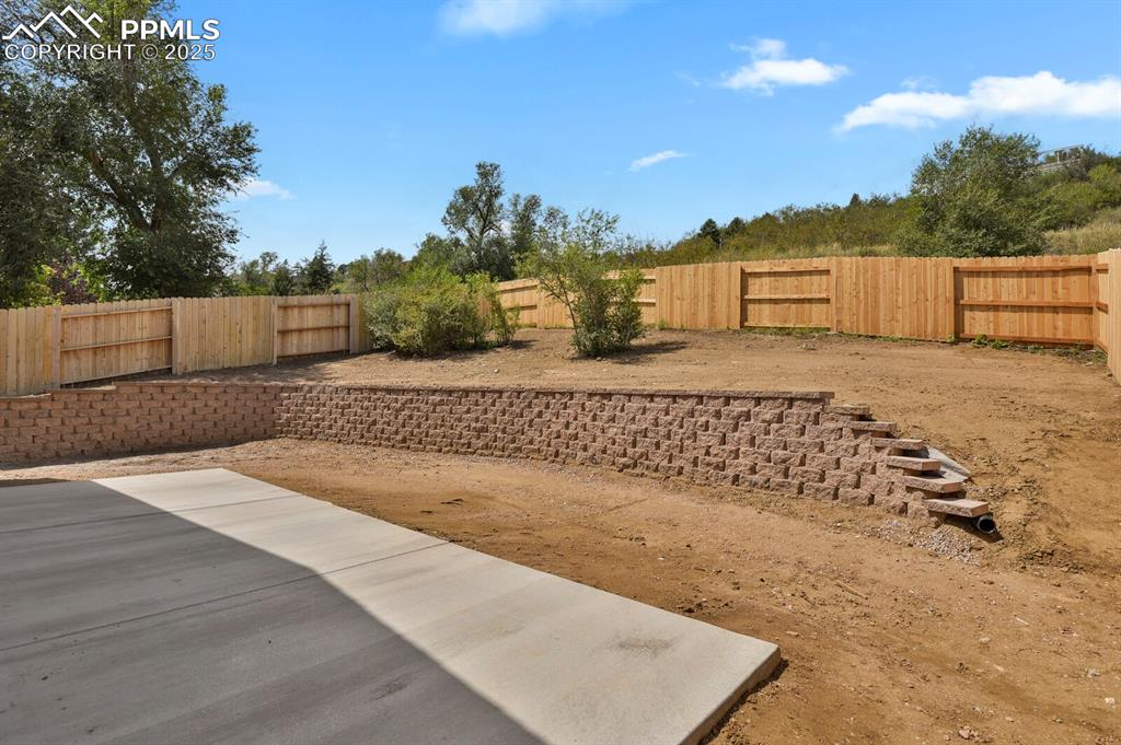 Image 31 of 49: Spacious concrete patio, retaining walls, and rear fencing