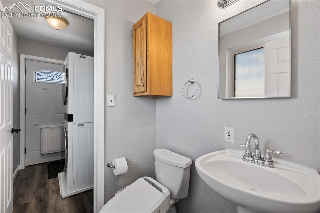 Image 17 of 38: Half bathroom featuring estacked washer and dryer, a sink, wood finished fl
