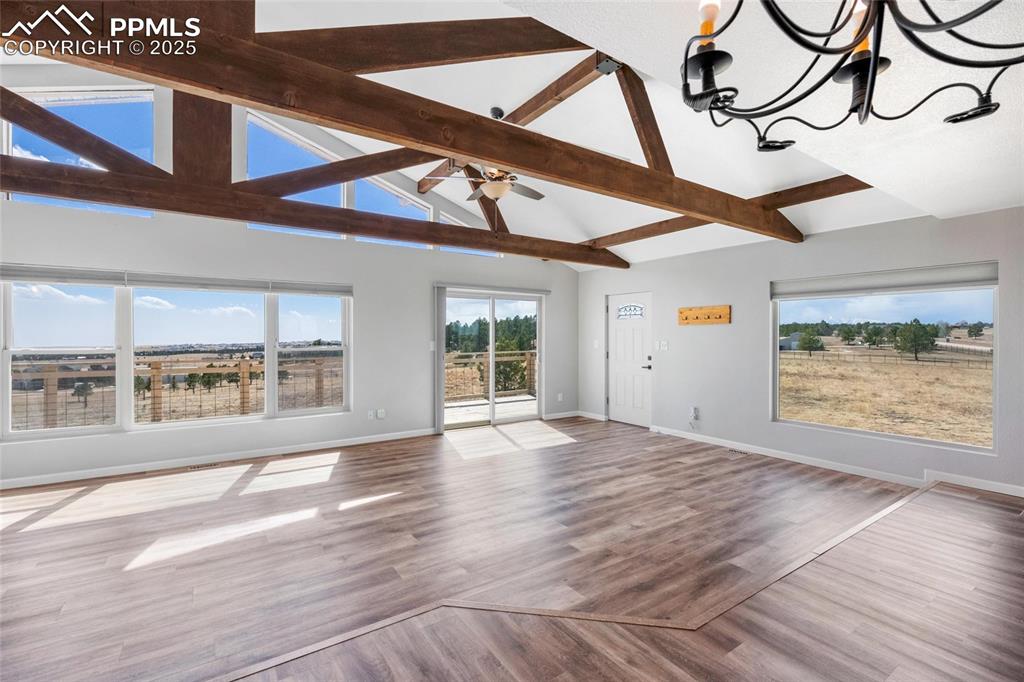 Image 6 of 38: Unfurnished living room with beam ceiling, baseboards, a chandelier, wood f