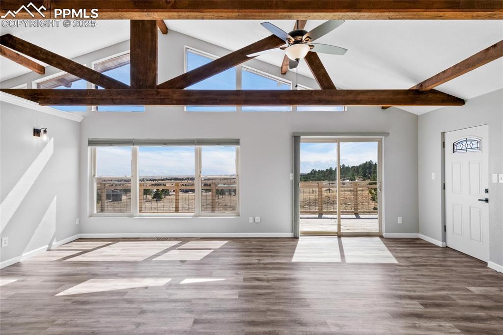 Image 9 of 38: Unfurnished living room with beamed ceiling, baseboards, ceiling fan, wood 