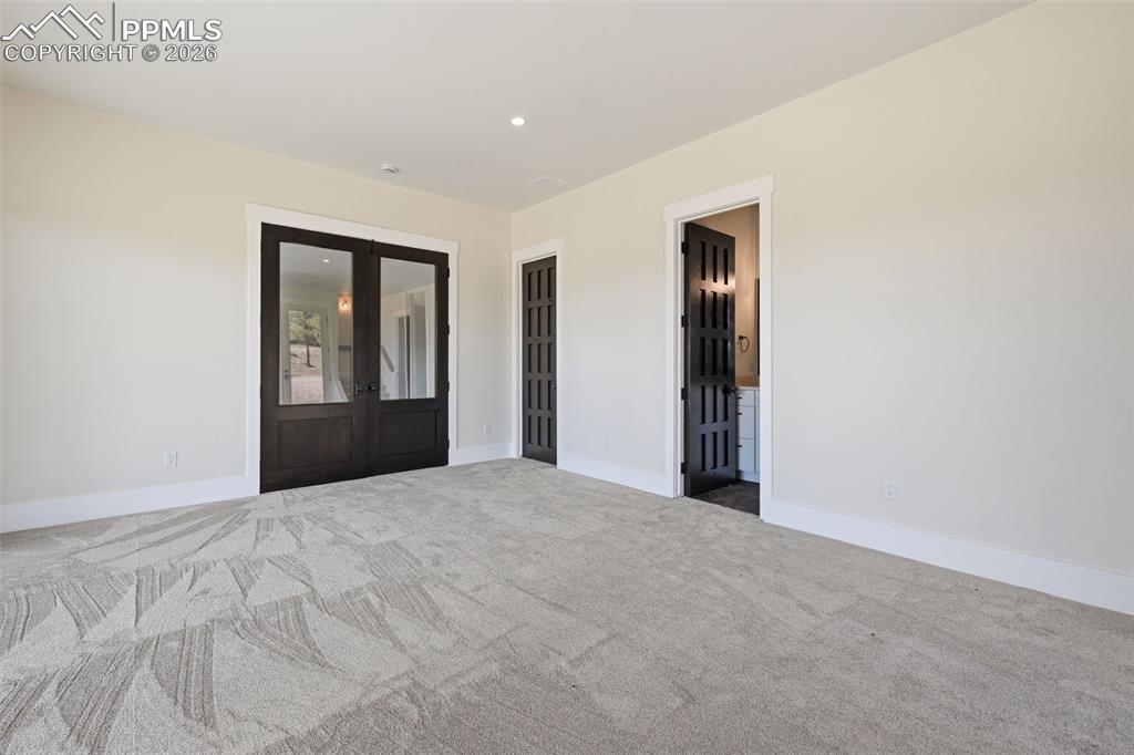 Image 39 of 45: Empty room with french doors, dark colored carpet, and recessed lighting