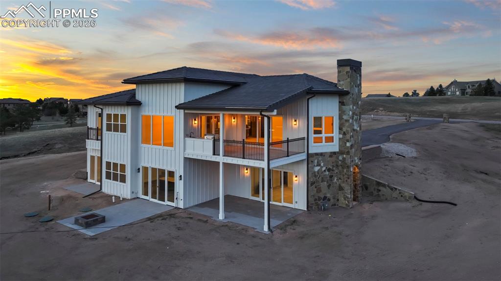 Image 7 of 45: Back of property at dusk featuring a patio, board and batten siding, a chim