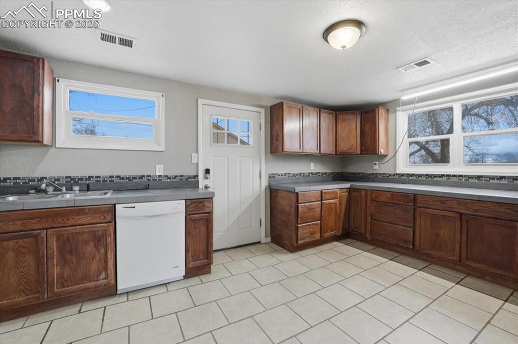 Image 12 of 24: Kitchen featuring white dishwasher, a textured ceiling, brown cabinets, and