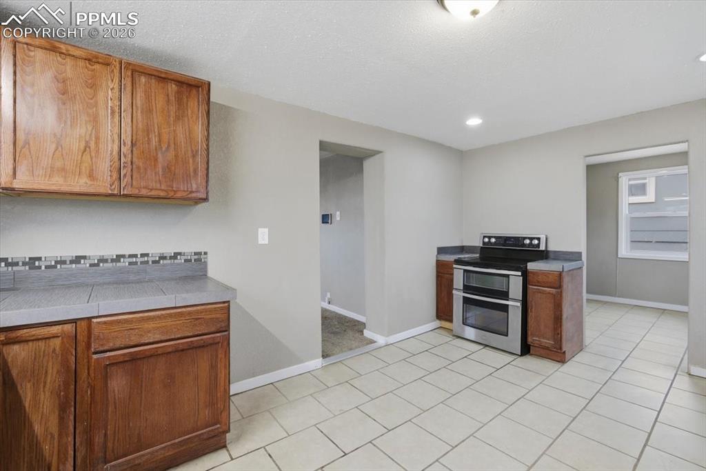 Image 13 of 24: Kitchen featuring range with two ovens, brown cabinets, light tile patterne