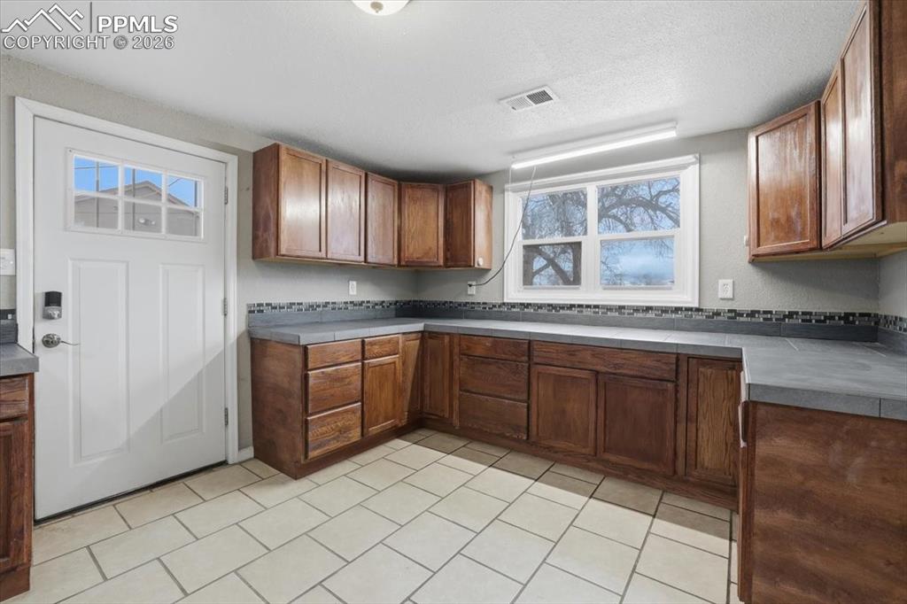 Image 14 of 24: Kitchen featuring brown cabinetry, dark countertops, a textured ceiling, an