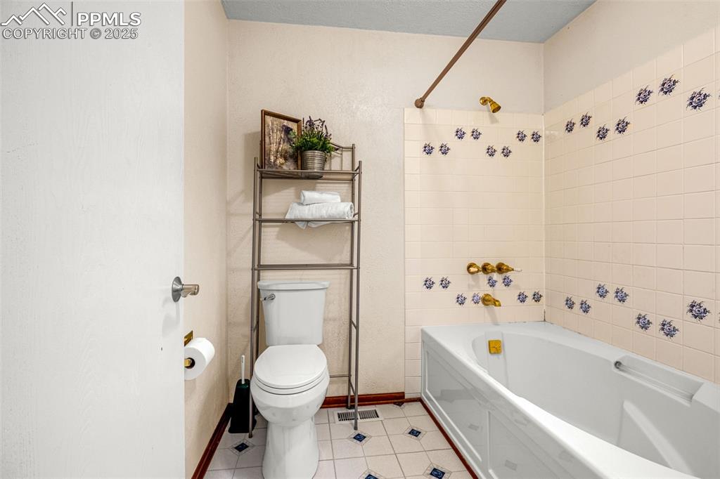 Image 18 of 38: Bathroom with toilet, tile patterned floors, tub / shower combination, and
