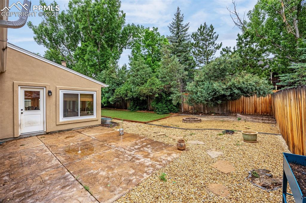 Image 28 of 38: Fenced backyard with a fire pit and a patio