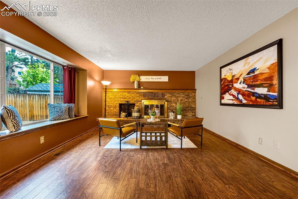 Image 9 of 38: Living room with wood finished floors, baseboards, and a brick fireplace