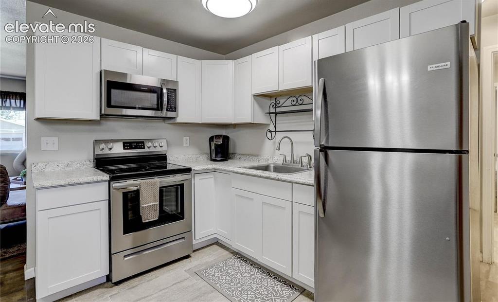 Image 7 of 17: Kitchen featuring white cabinetry, stainless steel appliances, speckled cou