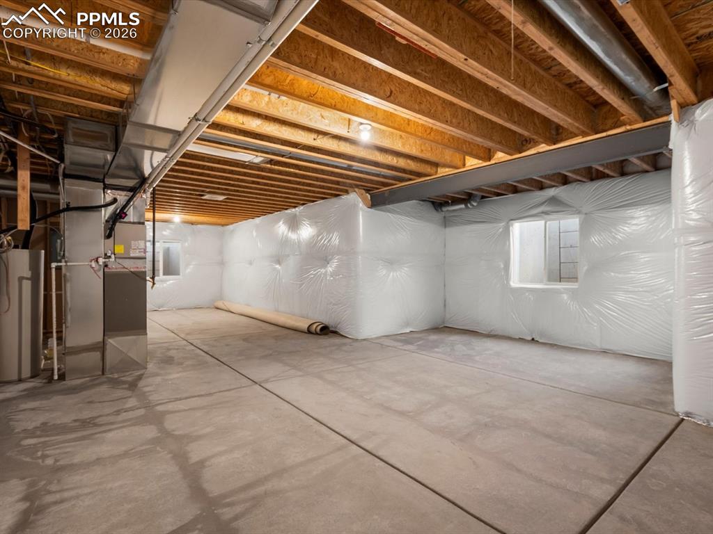 Image 24 of 45: The unfinished basement features concrete flooring, exposed ceiling joists,