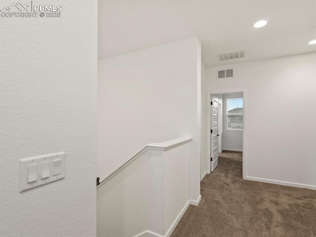 Image 29 of 45: The property includes a hallway with light brown carpeting, white walls, an