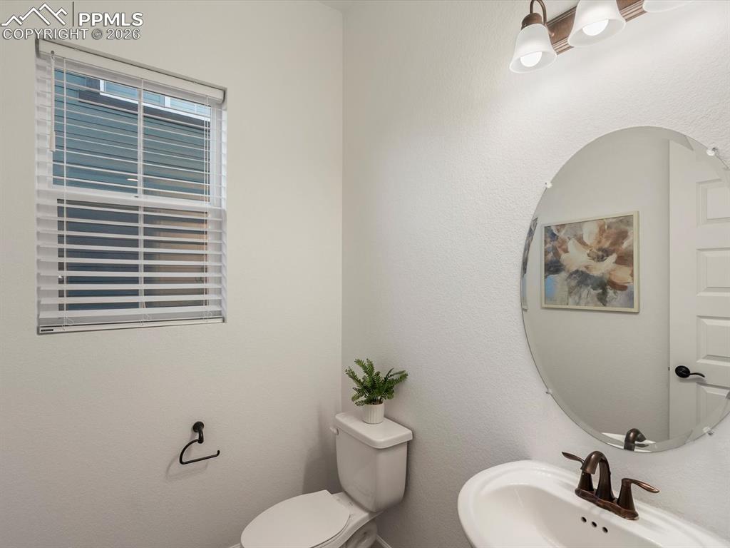 Image 7 of 45: The bathroom features an oval mirror, a white toilet, and a window with whi