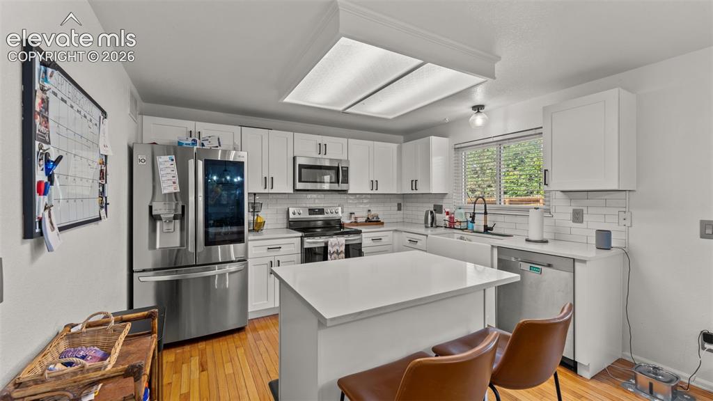 Image 10 of 34: White shaker cabinetry, stainless steel appliances, central island with sea