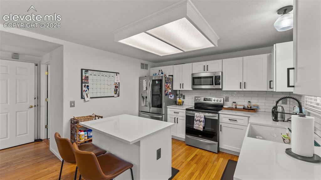 Image 12 of 34: Kitchen featuring wood-finish flooring, white cabinetry, integrated stainle
