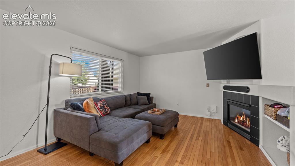 Image 7 of 34: Hardwood-style flooring, a large window with blinds, a corner fireplace wit