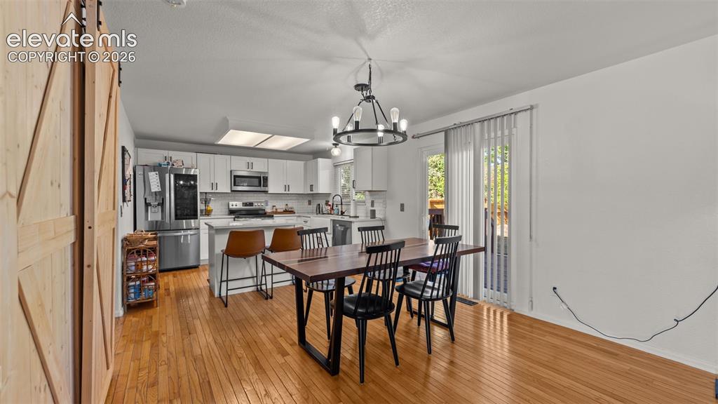 Image 8 of 34: Open-concept kitchen and dining area featuring hardwood flooring, white cab