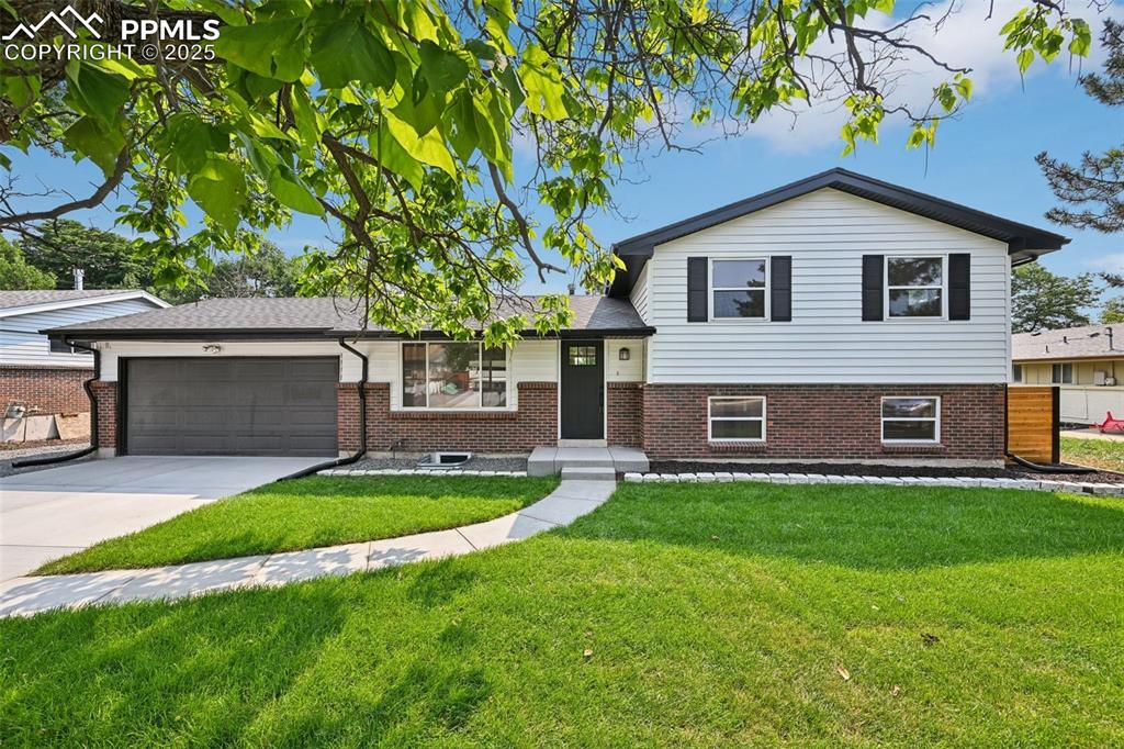 Caption: Split level home featuring brick siding, a garage, a front lawn, and concrete driveway