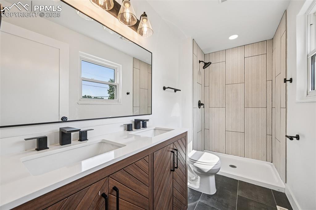 Image 19 of 49: Bathroom featuring double vanity, tiled shower, tile patterned flooring, an