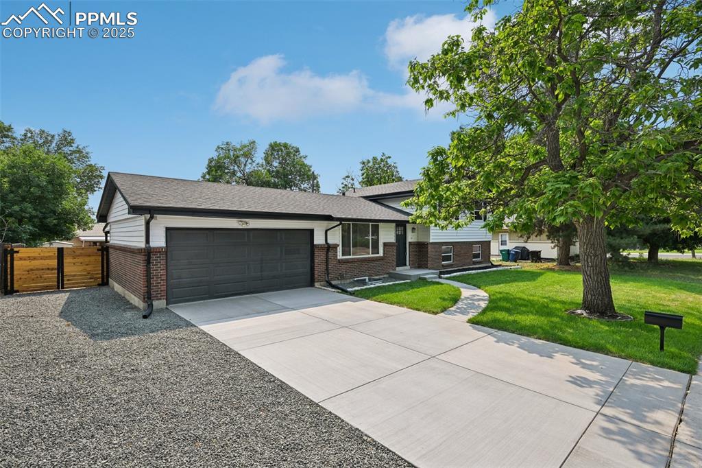Image 2 of 49: Split level home with brick siding, an attached garage, driveway, and a shi