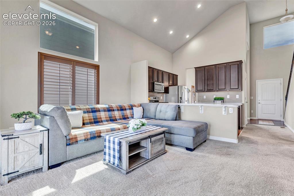 Image 13 of 38: Open-concept living area with vaulted ceilings, recessed lighting, carpet f