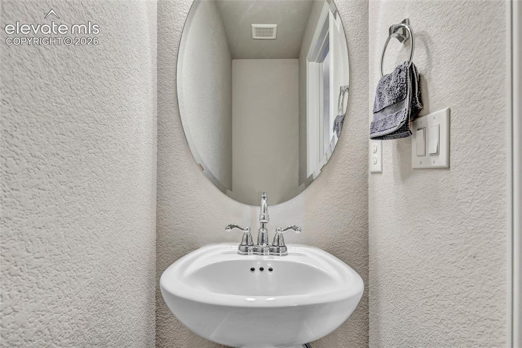 Image 15 of 38: Pedestal sink with chrome faucet, complemented by an oval mirror and textur
