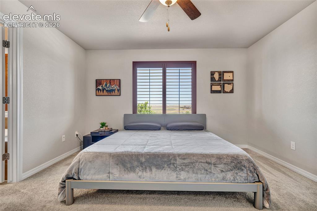 Image 17 of 38: Carpeted room with a ceiling fan and a window featuring wood-finish blinds