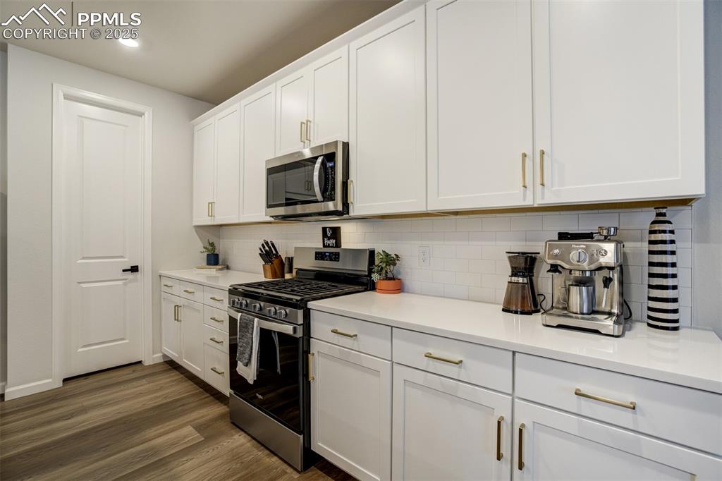Image 11 of 50: Kitchen featuring stainless steel appliances, white cabinetry, tasteful bac