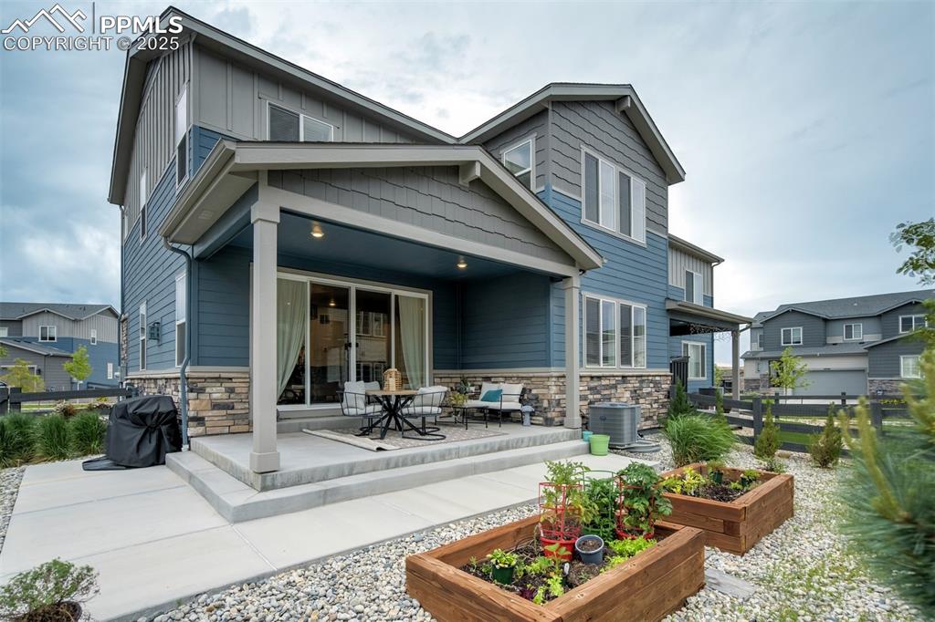 Image 43 of 50: Back of property featuring stone siding, a vegetable garden, a patio, and b