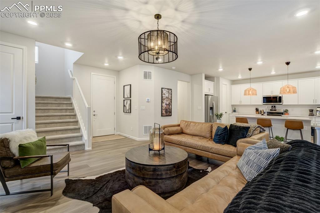Image 7 of 50: Living area with light wood finished floors, stairway, recessed lighting, a