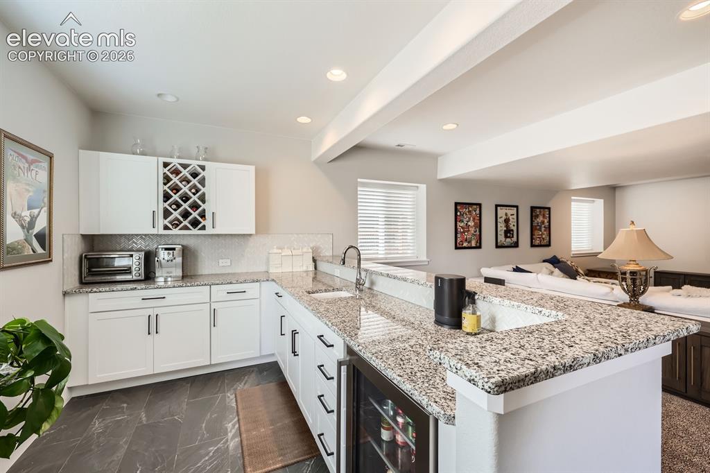 Image 26 of 38: Wet bar with granite countertops and beverage refrigerator.