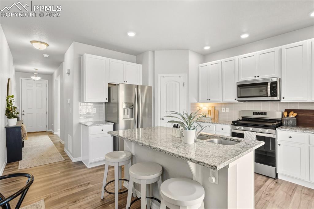 Image 12 of 37: Kitchen with stainless steel appliances, white cabinetry, light stone count