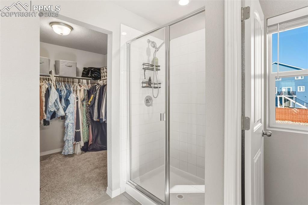 Image 19 of 37: Full bath featuring a walk in closet, light colored carpet, a shower stall,