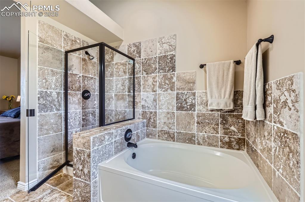 Image 15 of 28: Ensuite master bathroom featuring a bath, a shower stall, and Travertine ti