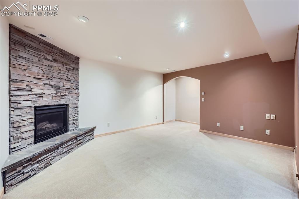 Image 22 of 28: Unfurnished family room with a stone fireplace, arched walkways, light colo