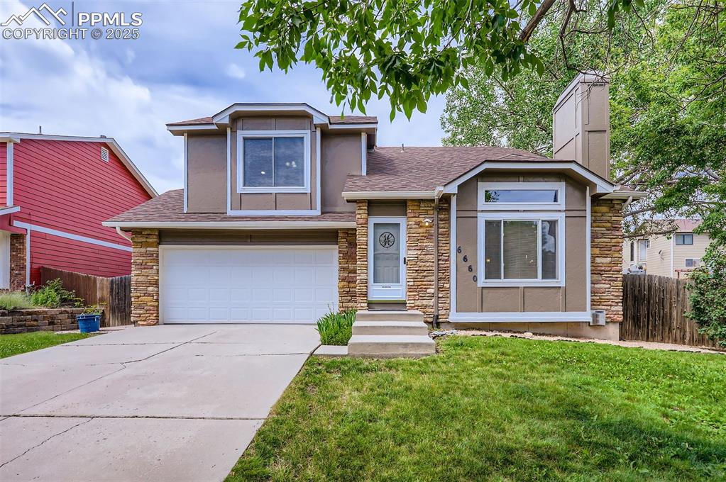 Image 3 of 28: Split level home with stone siding, an attached garage, stucco siding, and