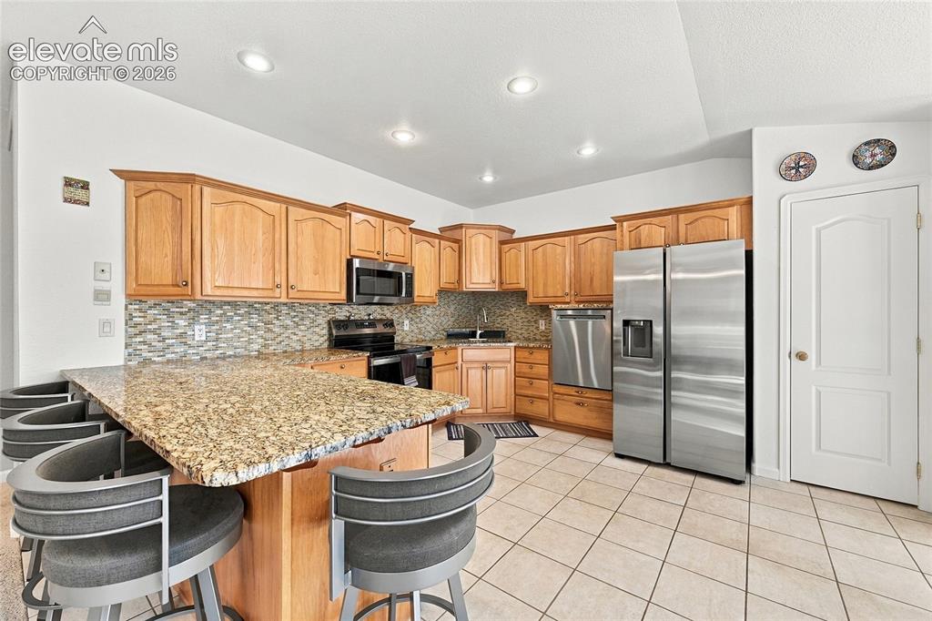 Image 12 of 36: Kitchen featuring a granite-topped island, light wood cabinetry, stainless