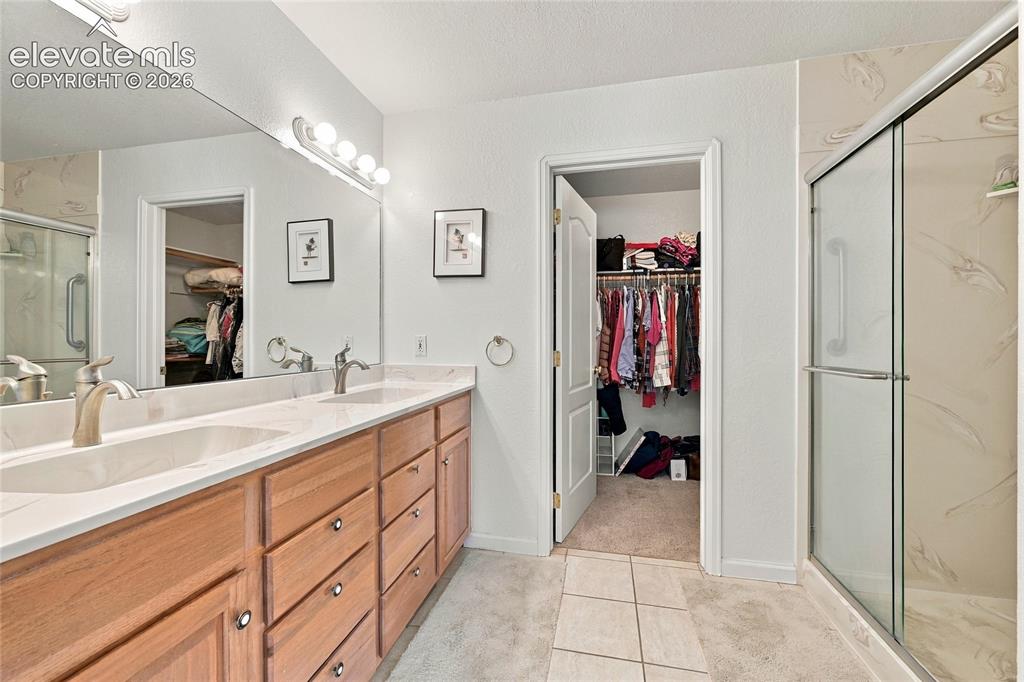 Image 16 of 36: Dual vanity with undermount sinks, wood-finish cabinetry, and a walk-in sho