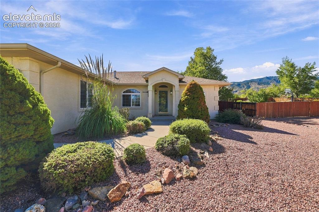 Image 2 of 36: Stucco exterior with an arched entryway, mature landscaping, and a concrete