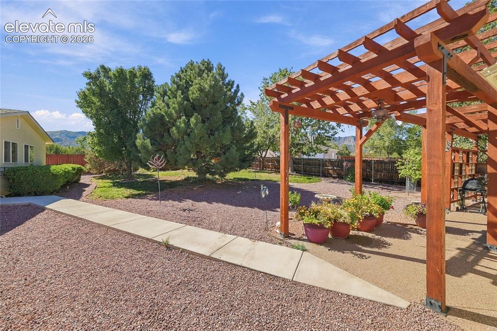 Image 24 of 36: Wood pergola with an integrated ceiling fan, concrete patio, and landscapin